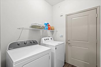 a laundry room with a washer and dryer next to a door at Stonepost Crossing Apartments, Overland Park